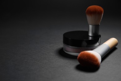 Photo of Face powder and makeup brushes on black background, closeup. Space for text