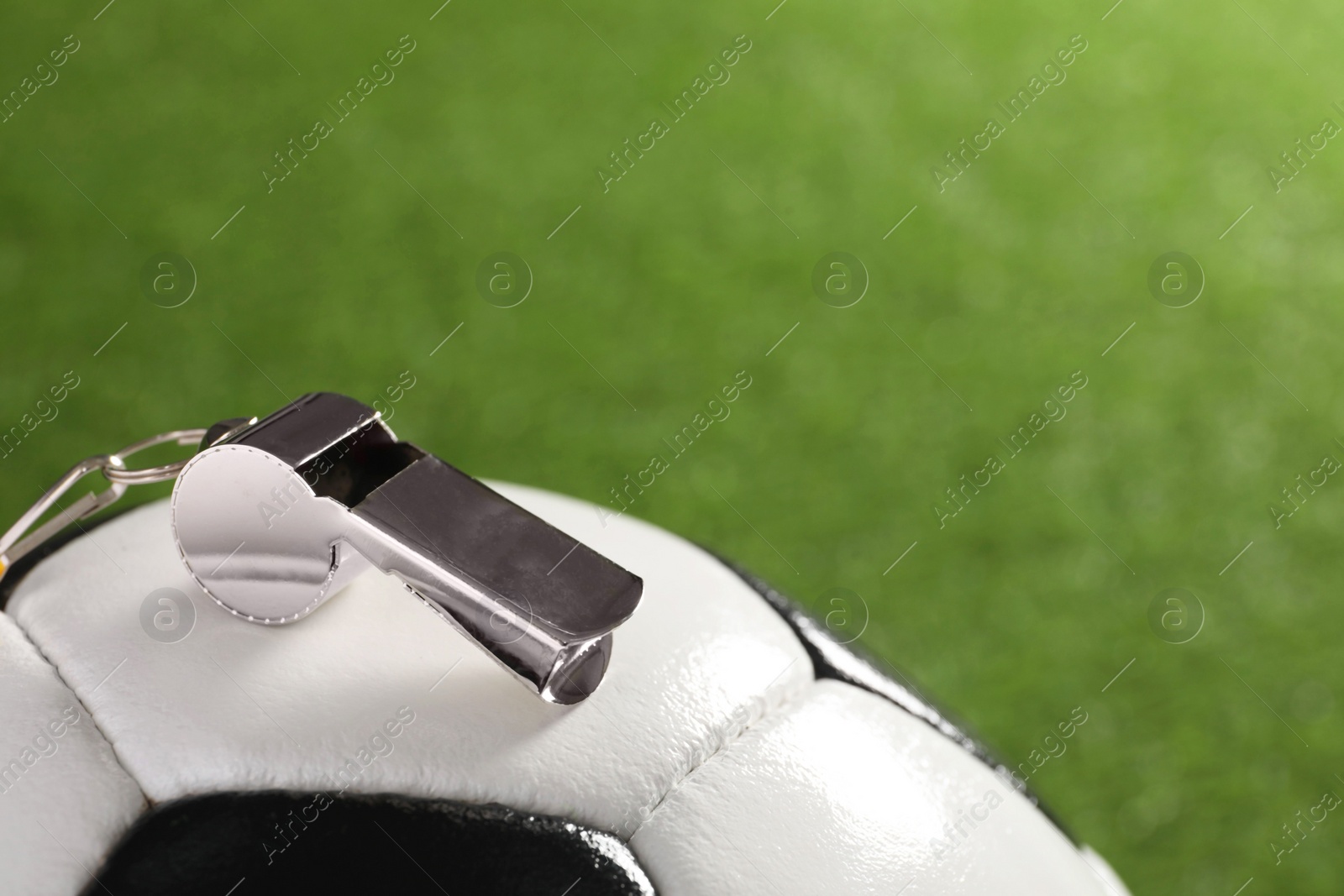 Photo of Football referee equipment. Soccer ball and metal whistle on green grass, closeup with space for text