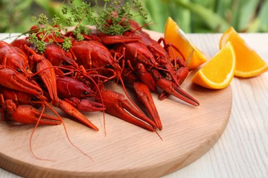 Photo of Delicious red boiled crayfish and orange on white wooden table, closeup