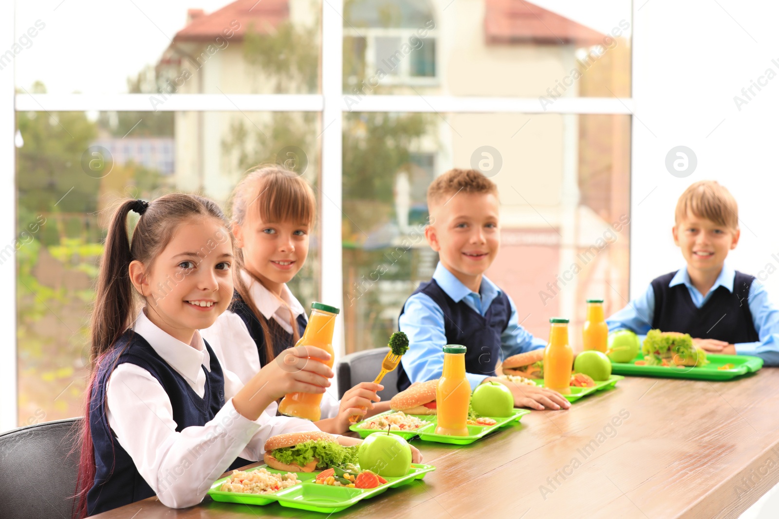 Photo of Happy children at table with healthy food in school canteen