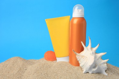 Photo of Sand with sunscreens and seashells against blue background, space for text. Sun protection care