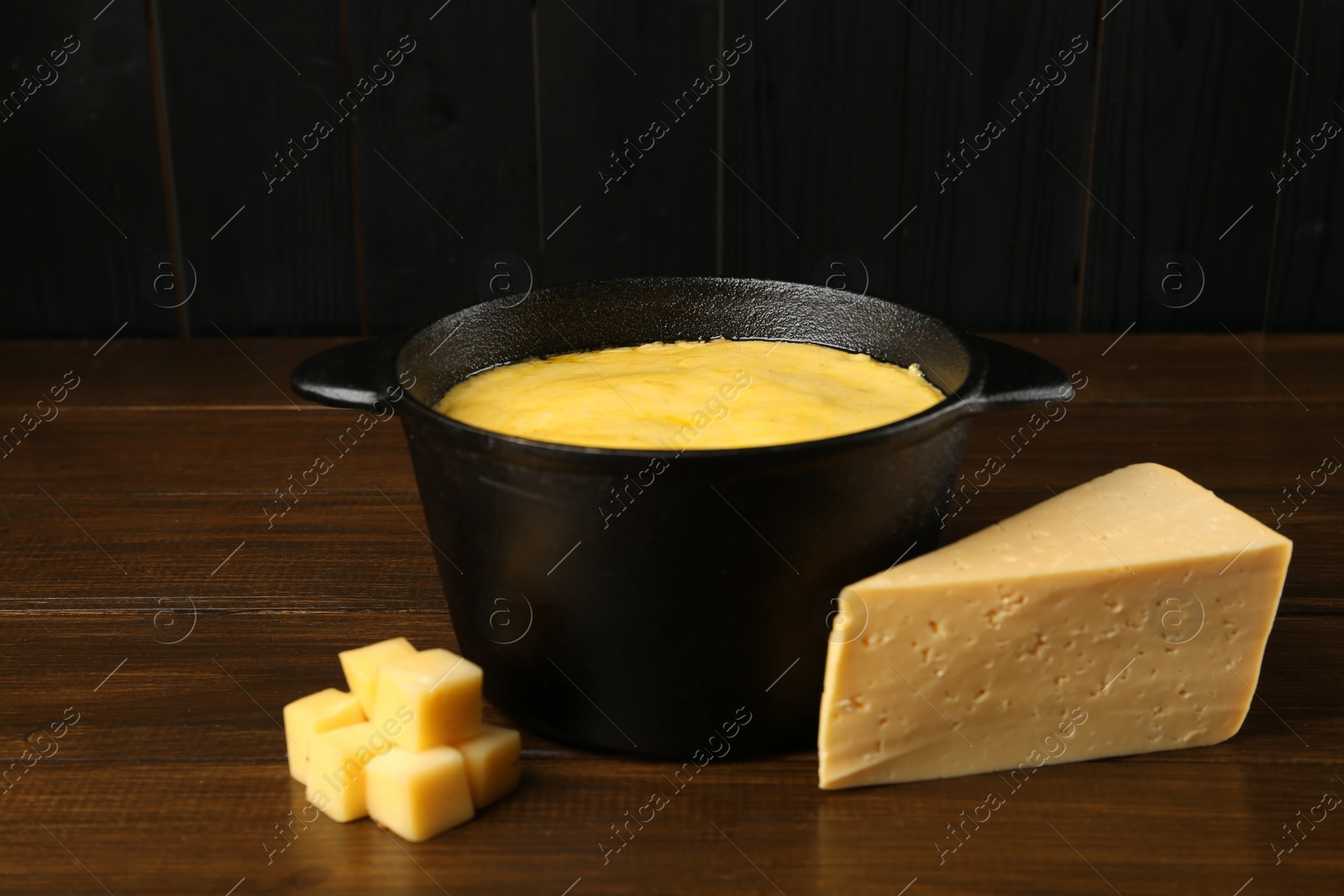 Photo of Fondue pot with melted cheese and pieces at wooden table