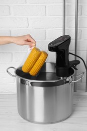 Photo of Woman putting vacuum packed corn into pot, closeup. Sous vide cooking