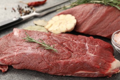 Piece of raw beef meat with rosemary on grey table, closeup