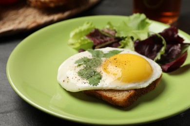 Plate with tasty fried egg, slice of bread and salad on black table, closeup