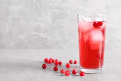 Tasty cranberry juice with ice cubes in glass and fresh berries on light grey table, space for text