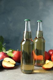 Photo of Delicious cider and apples with green leaves on gray table, closeup