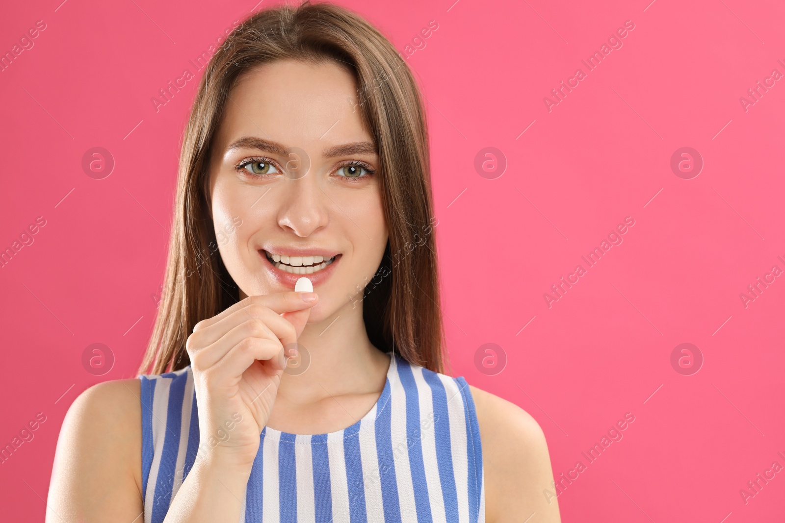 Photo of Young woman taking vitamin pill on pink background