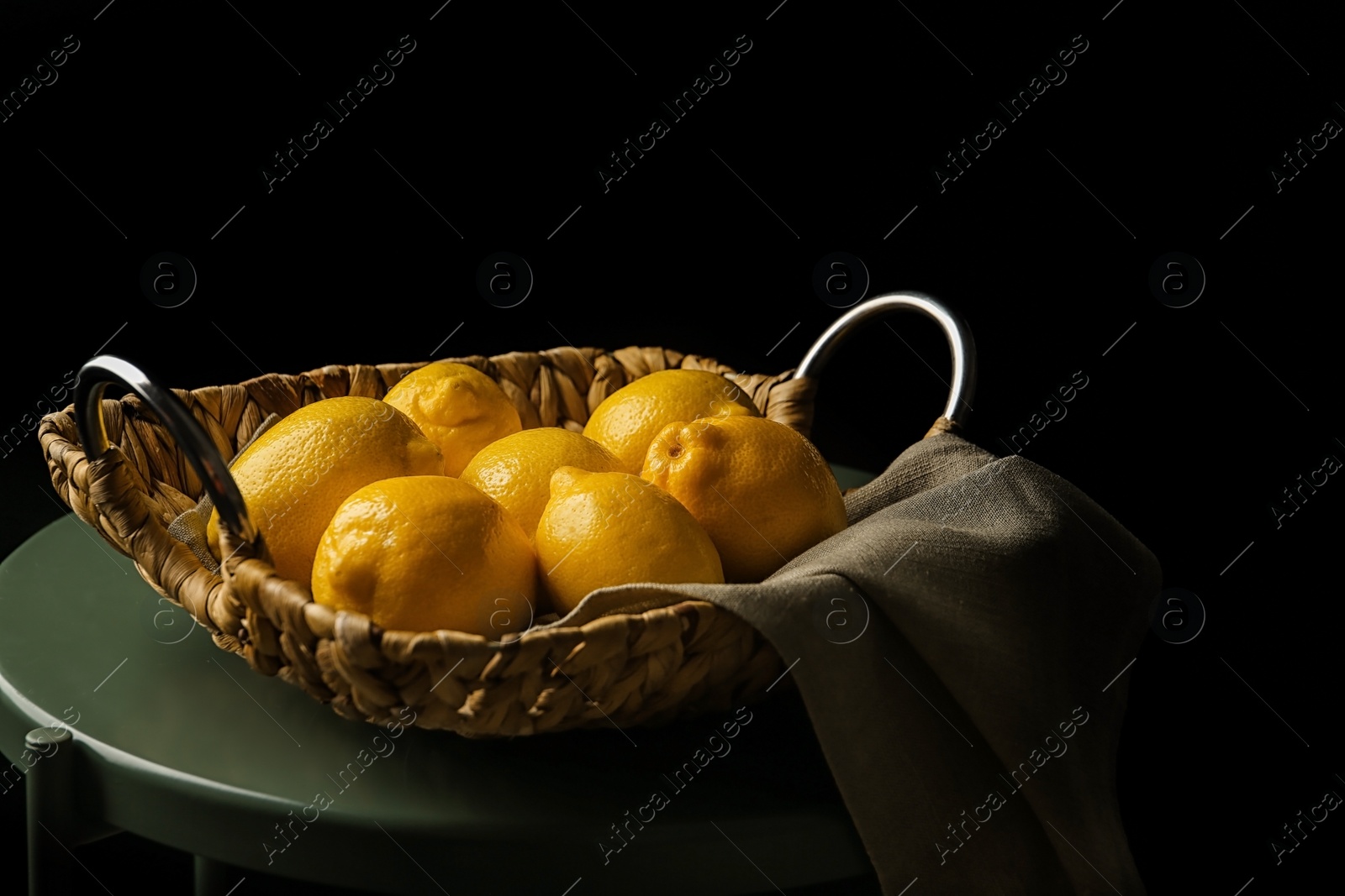 Photo of Basket with whole lemons on small table against dark background