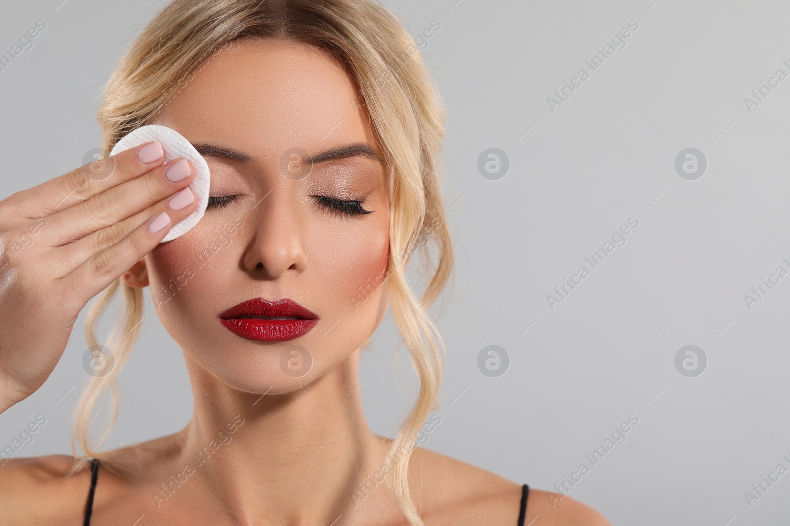 Photo of Beautiful woman removing makeup with cotton pad on light grey background, closeup. Space for text