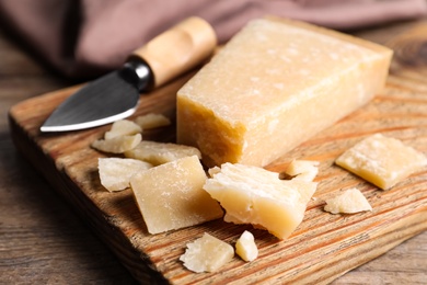 Photo of Parmesan cheese with knife on wooden table, closeup