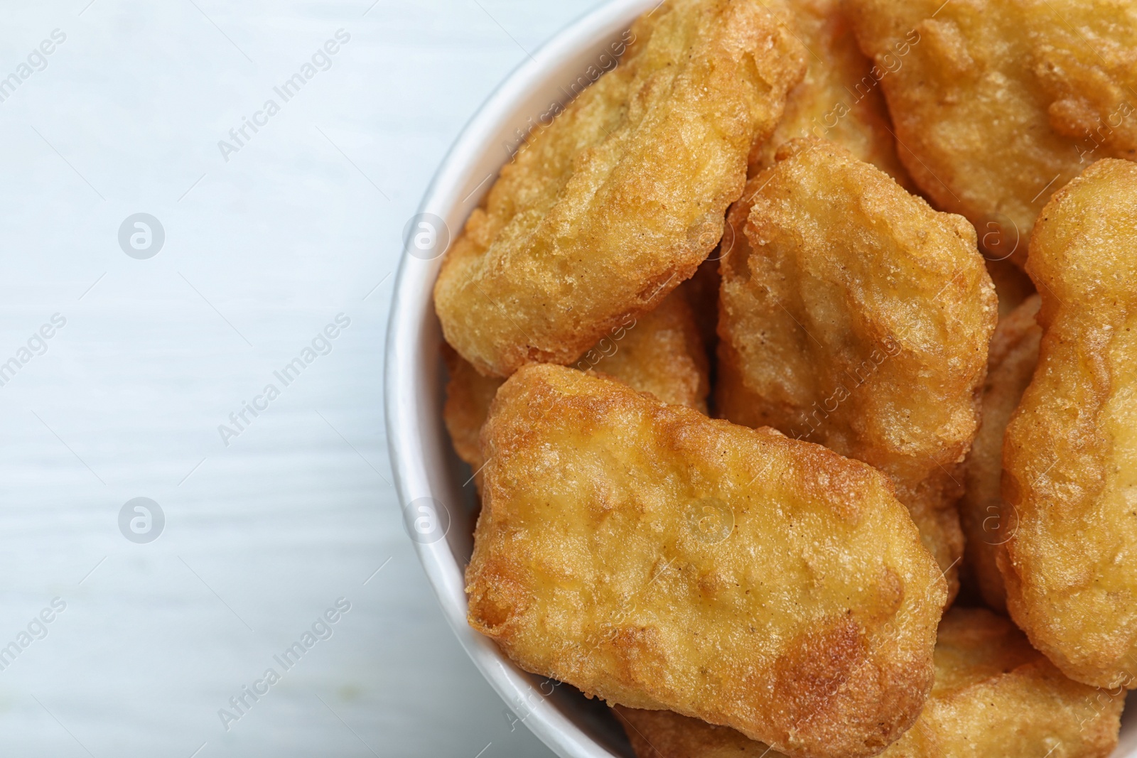 Photo of Bucket with tasty chicken nuggets on white wooden table, top view