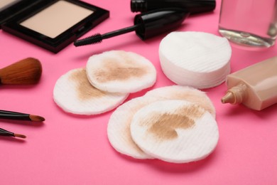 Photo of Dirty cotton pads after removing makeup and different cosmetic products on pink background, closeup