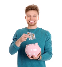 Photo of Happy young man with money and piggy bank on white background