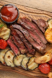 Photo of Delicious grilled beef with vegetables and tomato sauce on wooden table, top view