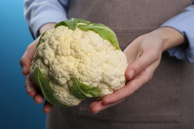 Woman holding fresh cauliflower against blue background, closeup