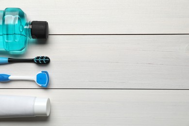 Photo of Tongue cleaner, toothbrush, paste and mouthwash on white wooden table, flat lay. Space for text