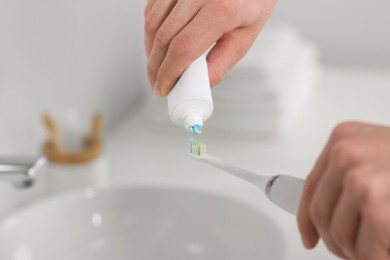 Photo of Man squeezing toothpaste from tube onto electric toothbrush in bathroom, closeup
