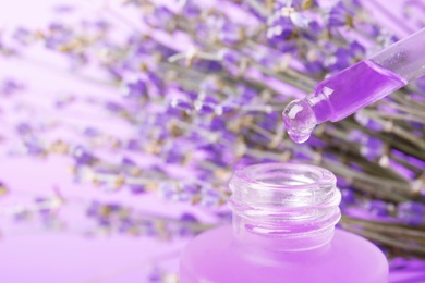 Photo of Dripping natural lavender oil into bottle against blurred background, closeup. Space for text