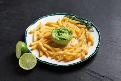 Photo of Plate with french fries, lime, avocado dip and rosemary on black table