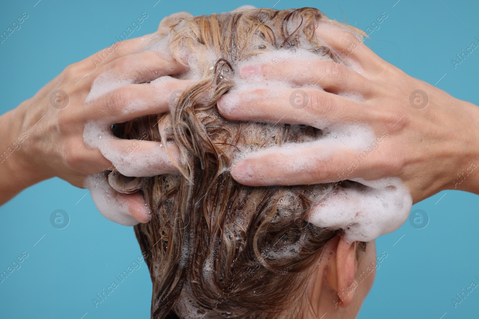 Photo of Woman washing hair on light blue background, closeup