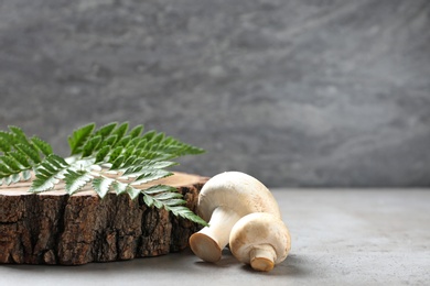 Photo of Fresh champignon mushrooms with wooden stump and leaf on table, space for text
