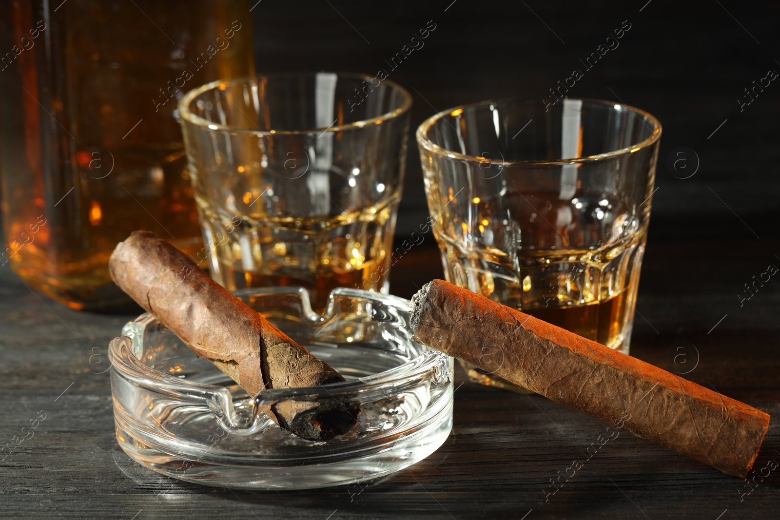 Photo of Cigars, ashtray and whiskey on black wooden table, closeup