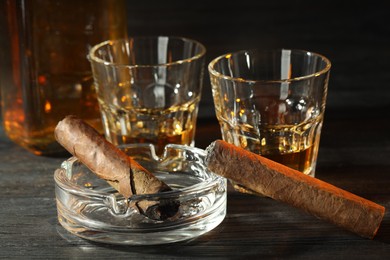 Photo of Cigars, ashtray and whiskey on black wooden table, closeup