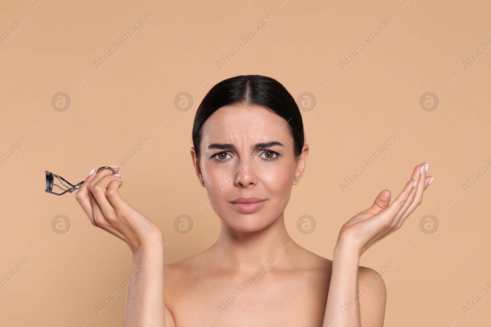 Photo of Emotional young woman with eyelash curler on beige background