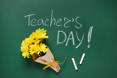 Photo of Flat lay composition with flowers and inscription TEACHER'S DAY on green chalkboard
