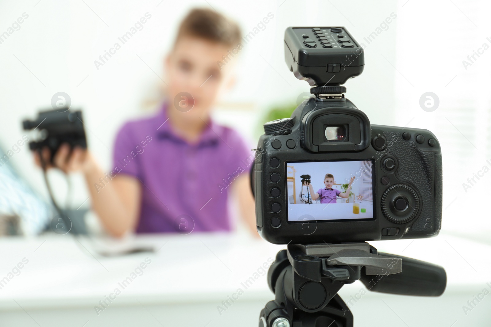 Photo of Cute little blogger with binoculars recording video at home, focus on camera