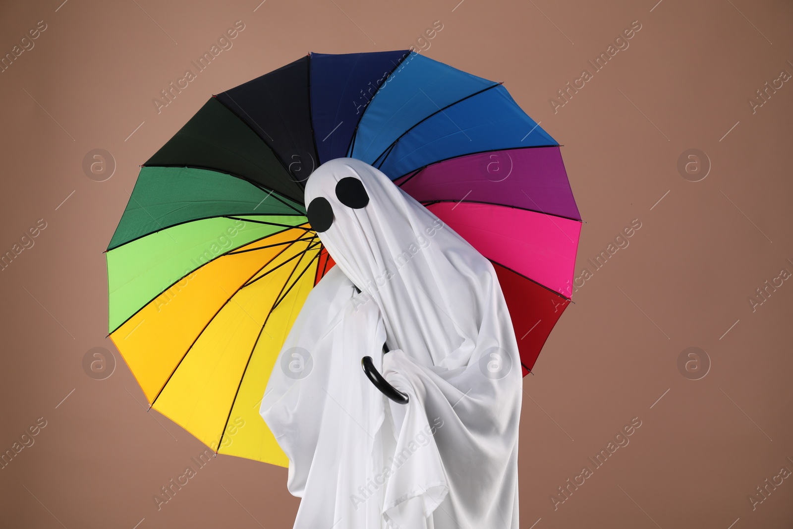 Photo of Person in ghost costume with rainbow umbrella on dark beige background