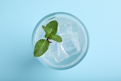 Photo of Glass of soda water with ice and mint on turquoise background, top view