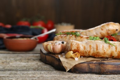 Tasty fresh grilled sausages with vegetables on wooden table, closeup. Space for text