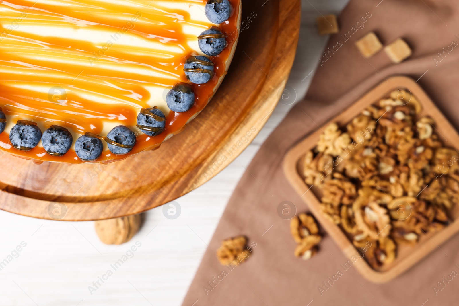 Photo of Delicious cheesecake with caramel and blueberries on white wooden table, top view. Space for text