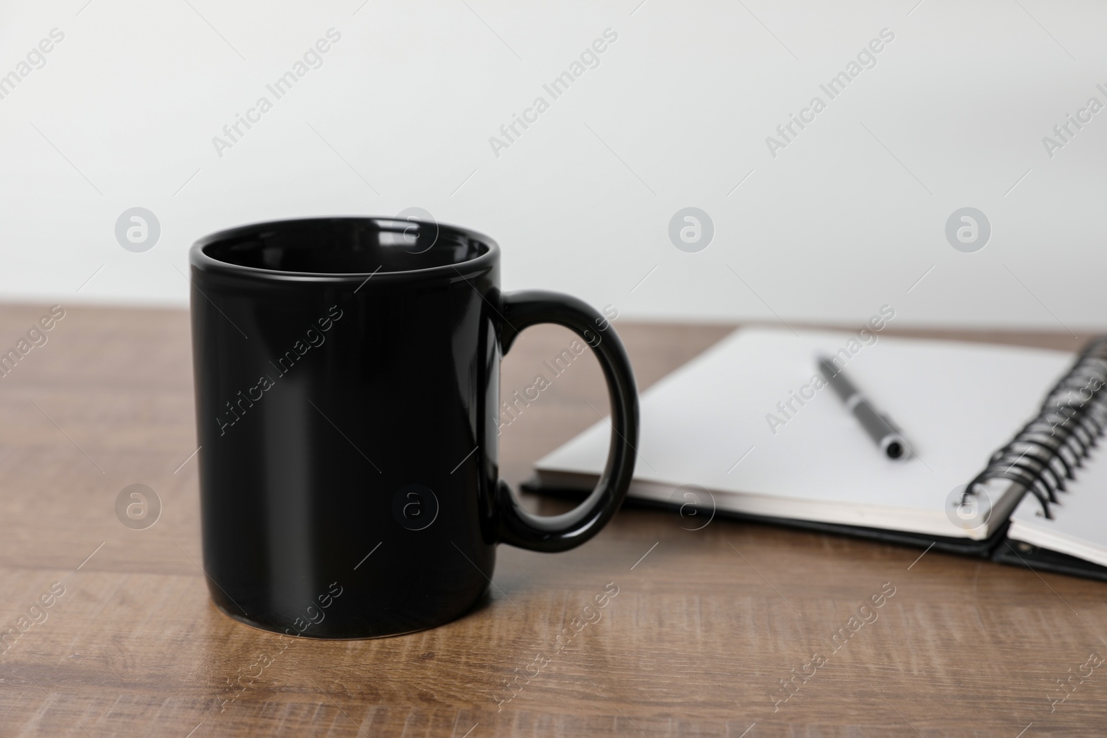 Black ceramic mug, notebook and pen on wooden table Photo of Black ceramic mug, notebook and pen on wooden table
