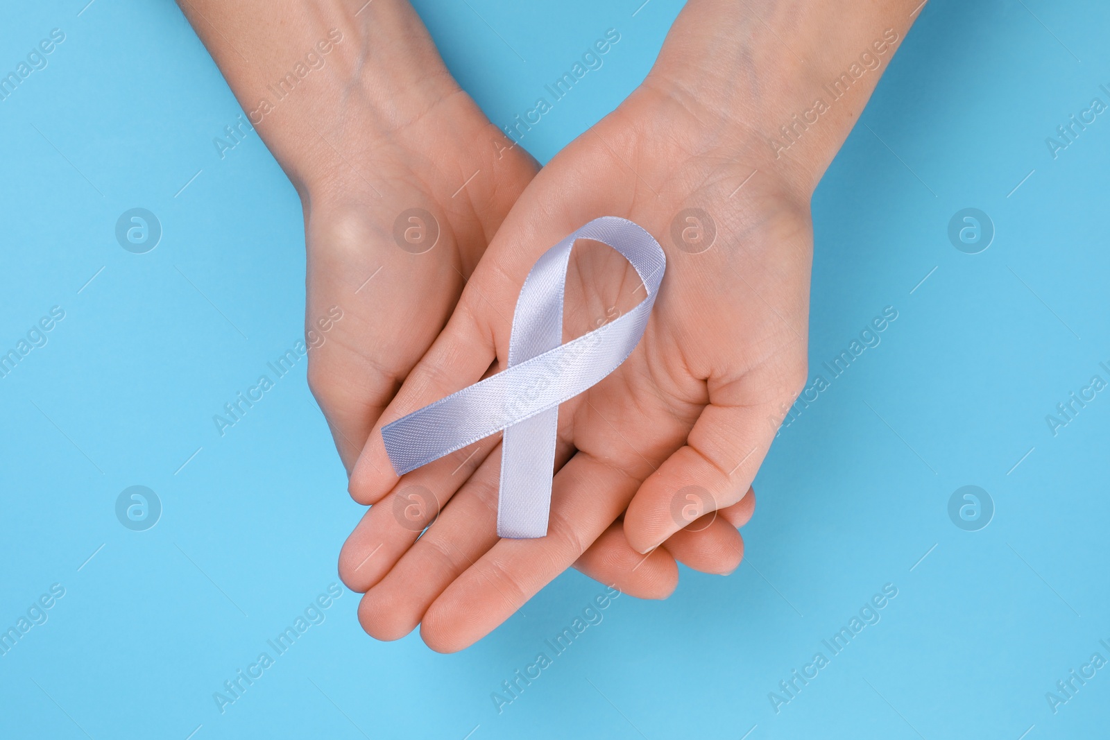 Photo of International Psoriasis Day. Woman with light blue ribbon as symbol of support on light blue background, top view