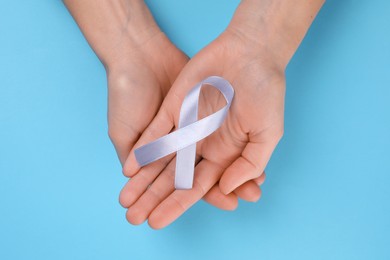 Photo of International Psoriasis Day. Woman with light blue ribbon as symbol of support on light blue background, top view
