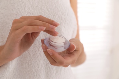 Photo of Woman holding jar with cream near window, closeup