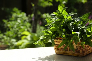 Beautiful green mint in wicker basket on white wooden table outdoors, space for text