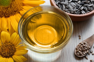 Photo of Sunflower oil in glass bowl and seeds on wooden table
