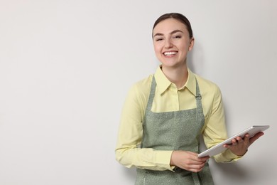 Beautiful young woman in clean apron with tablet on light grey background. Space for text