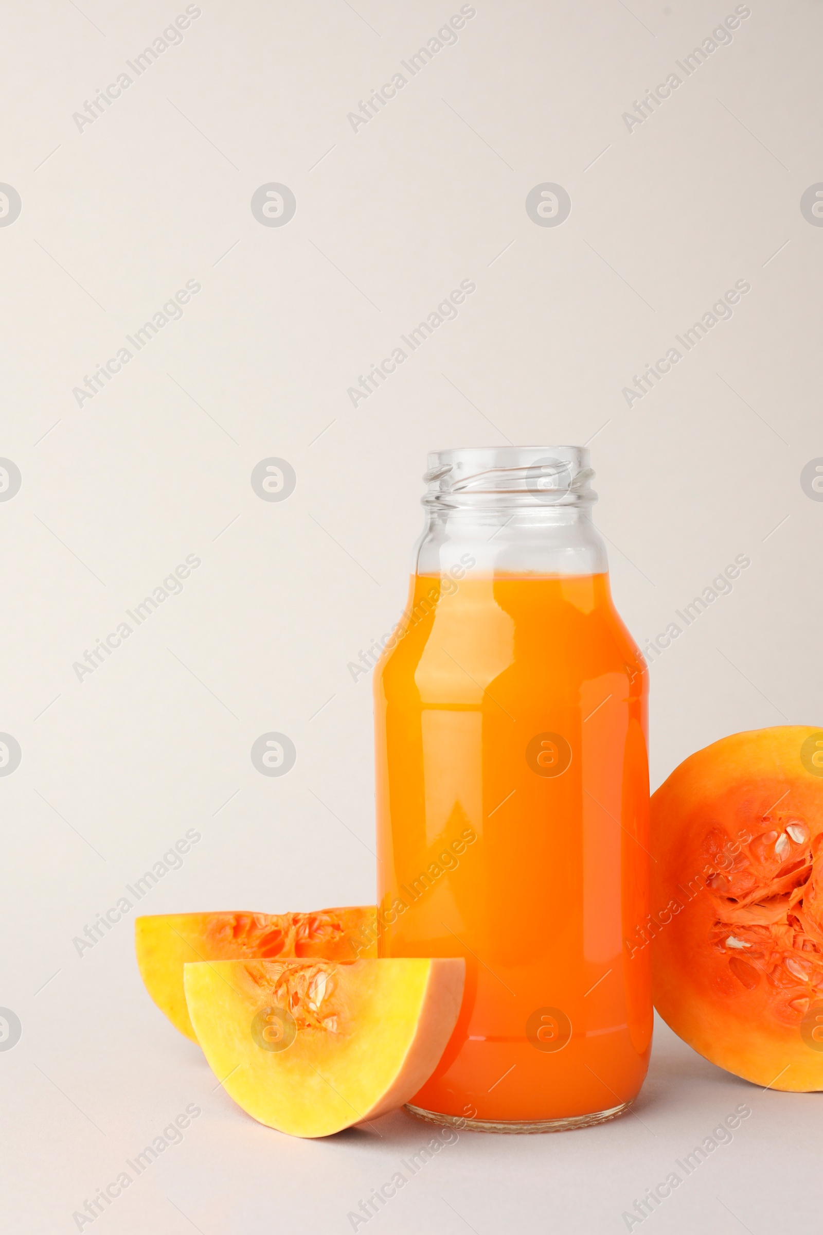 Photo of Tasty pumpkin juice in glass bottle and cut pumpkin on light background