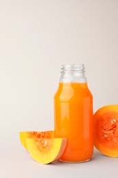 Photo of Tasty pumpkin juice in glass bottle and cut pumpkin on light background