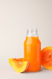 Tasty pumpkin juice in glass bottle and cut pumpkin on light background