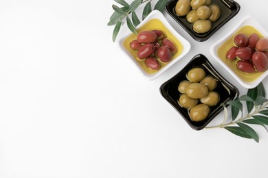 Photo of Bowls with different ripe olives and leaves on white background, flat lay. Space for text