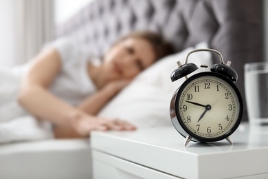 Alarm clock on nightstand of young woman suffering from headache
