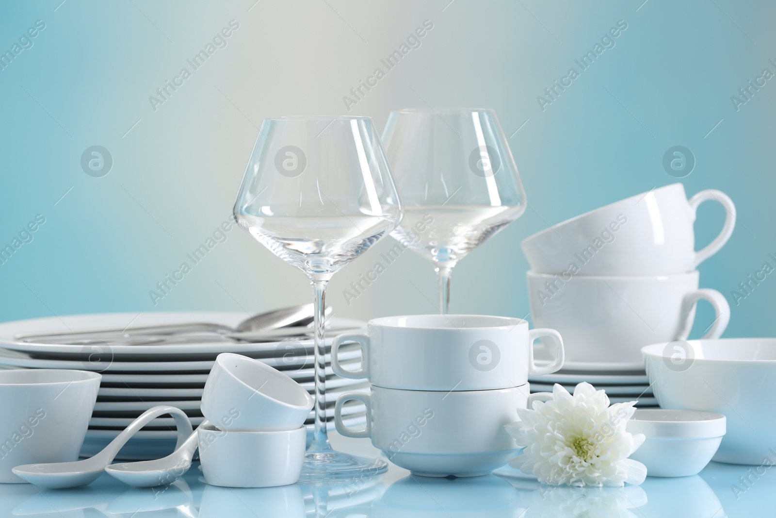 Photo of Set of many clean dishware, flower and glasses on light blue table