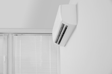Modern air conditioner on white wall indoors, low angle view. Space for text