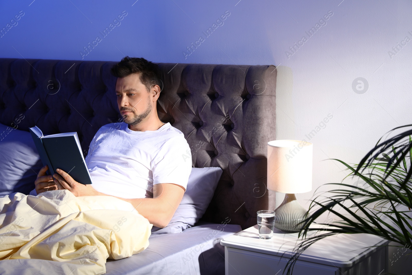 Photo of Handsome man reading book in dark room at night. Bedtime